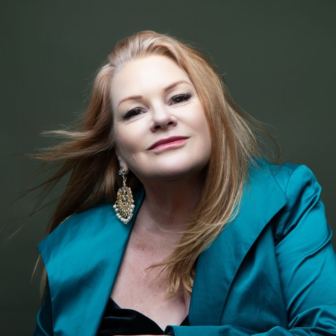Portrait of Dina Mande in a teal satin jacket, her hair in motion